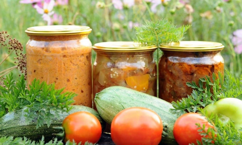 3 jars of home canned goods, sitting outside surrounded by fresh vegetables.