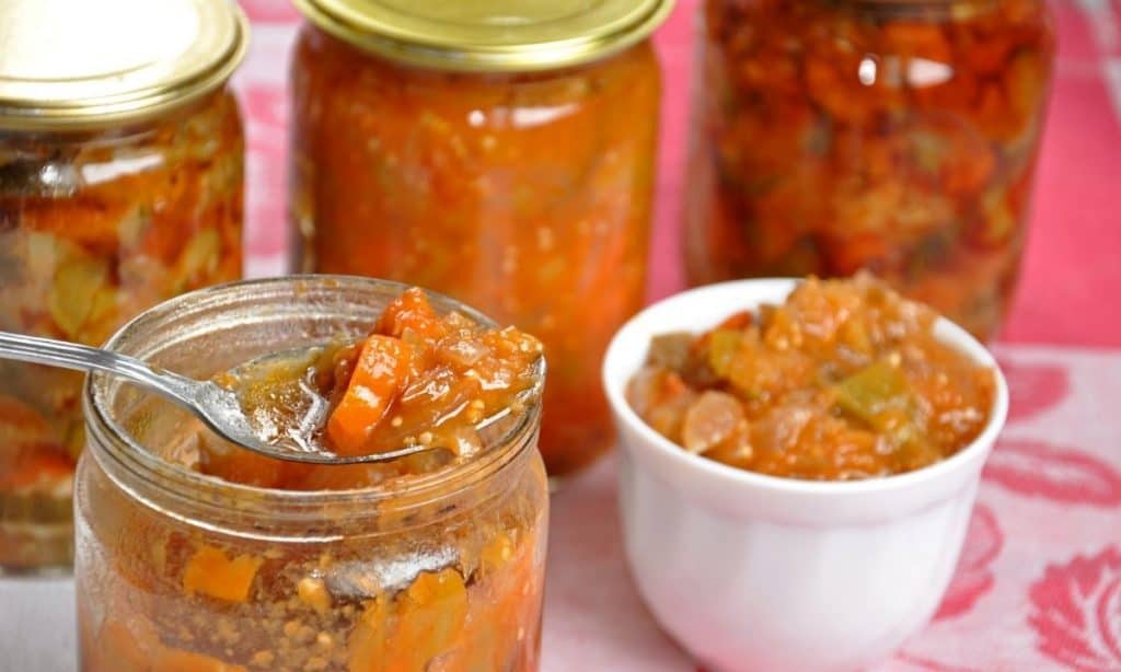 Jars of canned food, with one open and a spoon showing canned tomatoes. 