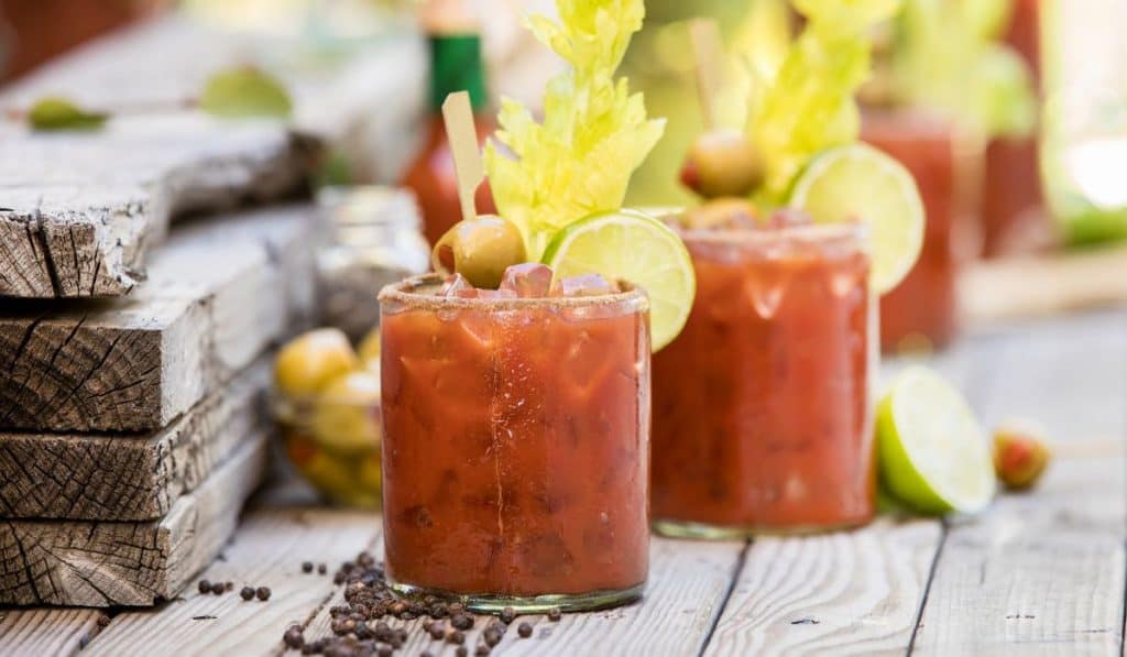 2 bloody Mary cocktails on a wood platform. 