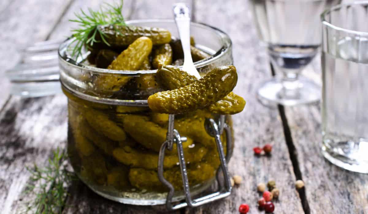 A jar of small pickles with peppercorns surrounding along with fresh dill. 
